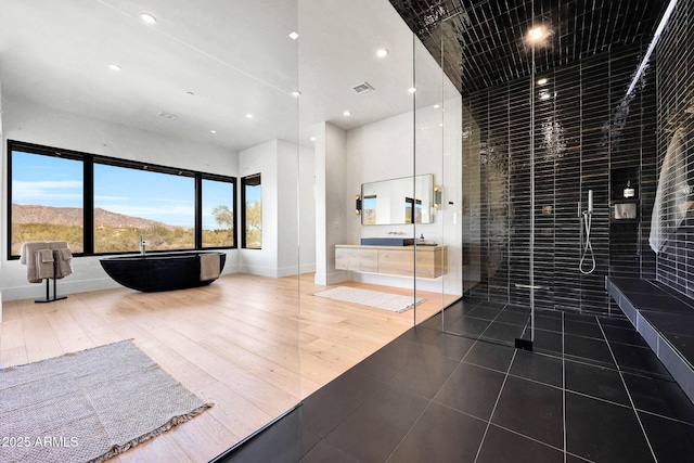 bathroom with plus walk in shower, a towering ceiling, wood-type flooring, vanity, and a mountain view