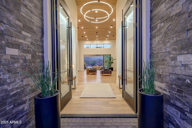 hallway with hardwood / wood-style flooring, brick wall, a towering ceiling, and french doors