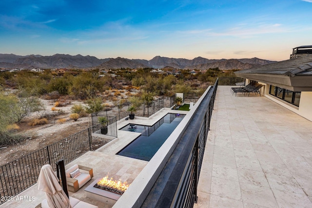 pool at dusk with a patio, a mountain view, and a fire pit