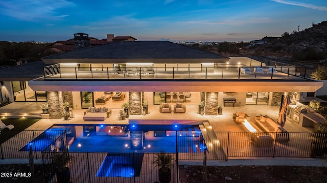 pool at dusk with area for grilling, a patio area, an outdoor living space with a fire pit, and an in ground hot tub