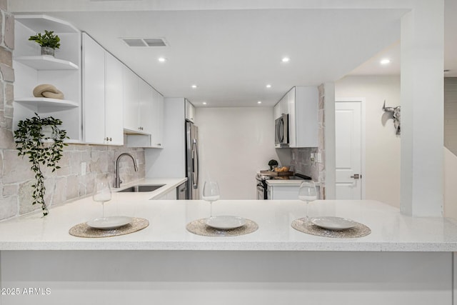 kitchen featuring white cabinets, stainless steel appliances, kitchen peninsula, decorative backsplash, and sink