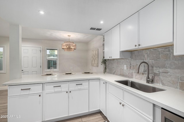 kitchen featuring kitchen peninsula, hanging light fixtures, backsplash, white cabinets, and sink