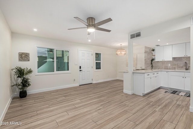 kitchen with sink, white cabinets, tasteful backsplash, ceiling fan with notable chandelier, and hanging light fixtures