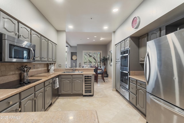 kitchen featuring sink, stainless steel appliances, kitchen peninsula, decorative backsplash, and beverage cooler