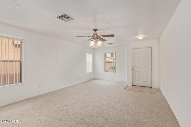 empty room with a ceiling fan, light colored carpet, visible vents, and baseboards