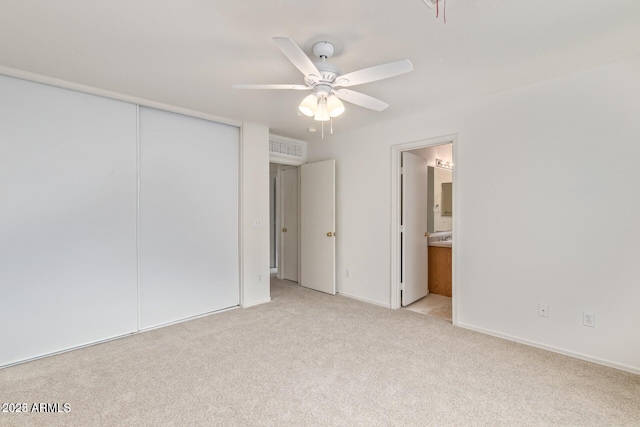 unfurnished bedroom featuring a closet, visible vents, light carpet, ensuite bathroom, and ceiling fan