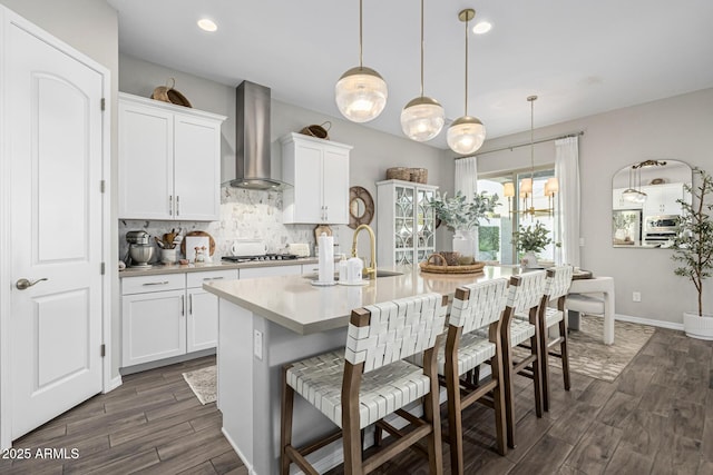 kitchen featuring white cabinets, decorative light fixtures, a kitchen island with sink, and wall chimney range hood