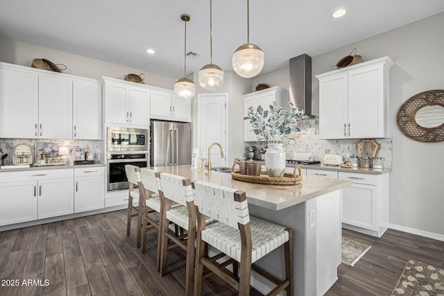 kitchen with pendant lighting, white cabinets, tasteful backsplash, wall chimney range hood, and stainless steel appliances