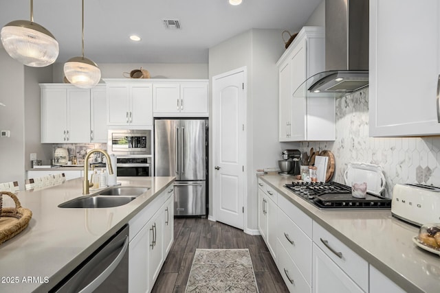 kitchen featuring appliances with stainless steel finishes, white cabinetry, hanging light fixtures, sink, and wall chimney exhaust hood