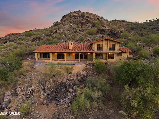 6349 E Hummingbird Ln, Paradise Valley, AZ 85253 - back of house at dusk featuring a tile roof, a chimney, a mountain view, stucco siding, and a patio