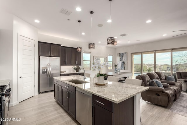 kitchen featuring sink, a kitchen island with sink, hanging light fixtures, stainless steel appliances, and dark brown cabinetry