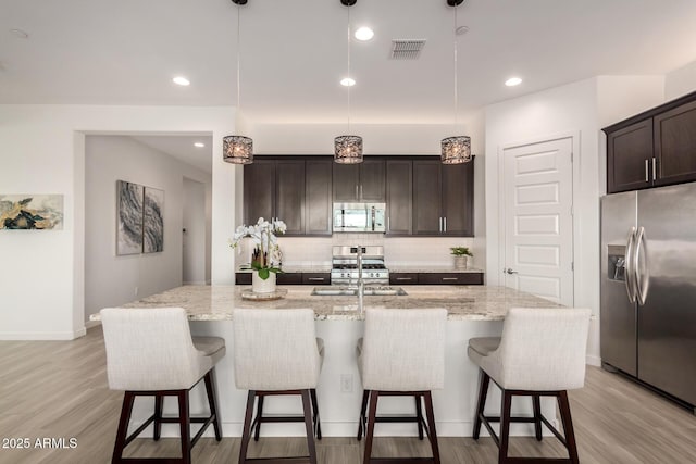 kitchen with a kitchen island with sink, decorative light fixtures, and stainless steel appliances