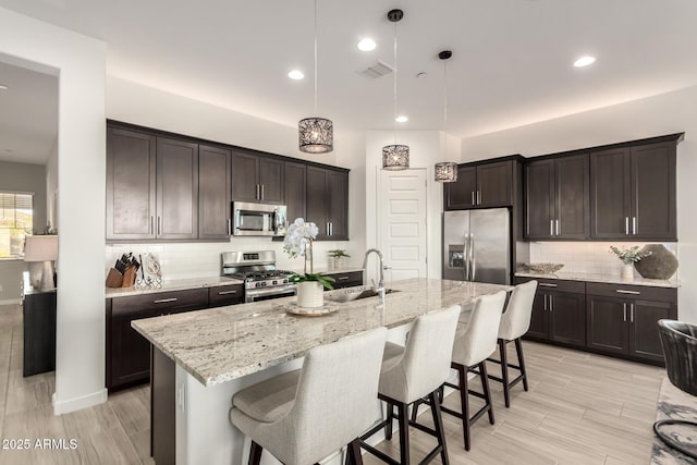 kitchen with hanging light fixtures, stainless steel appliances, sink, and a center island with sink