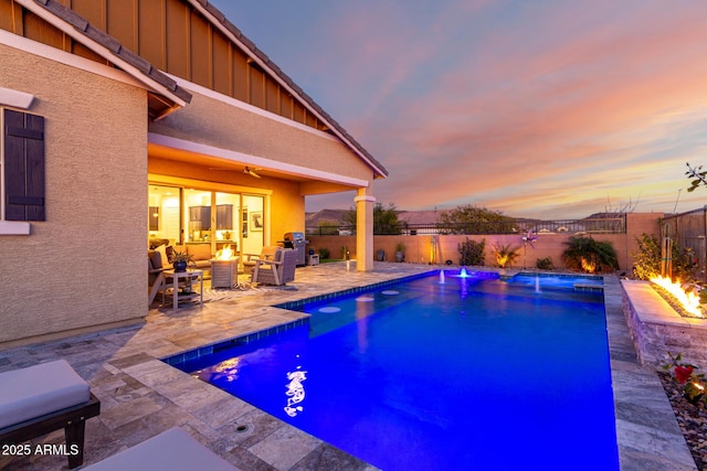 pool at dusk featuring pool water feature, ceiling fan, a patio area, and a fire pit