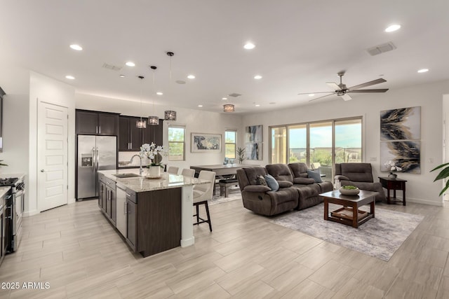 kitchen with stainless steel appliances, a wealth of natural light, an island with sink, a kitchen bar, and decorative light fixtures