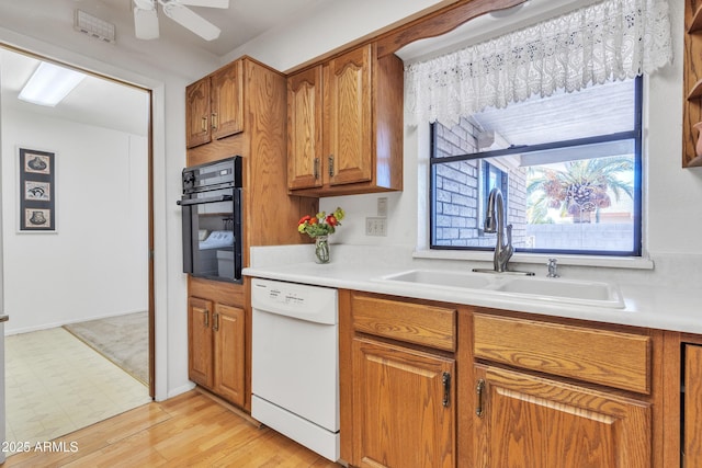 kitchen with white dishwasher, oven, a sink, light countertops, and brown cabinets