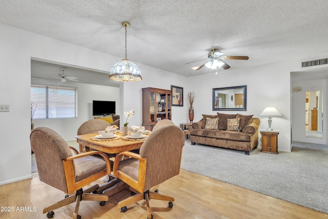 dining room featuring light wood-style floors, ceiling fan, visible vents, and a textured ceiling