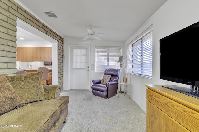 living area featuring baseboards, visible vents, a ceiling fan, light colored carpet, and brick wall