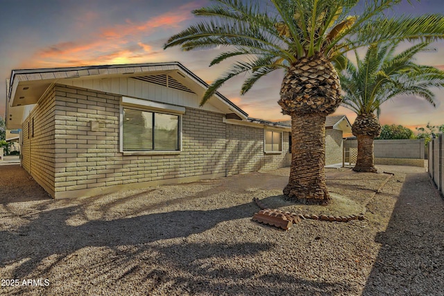 property exterior at dusk featuring brick siding and fence