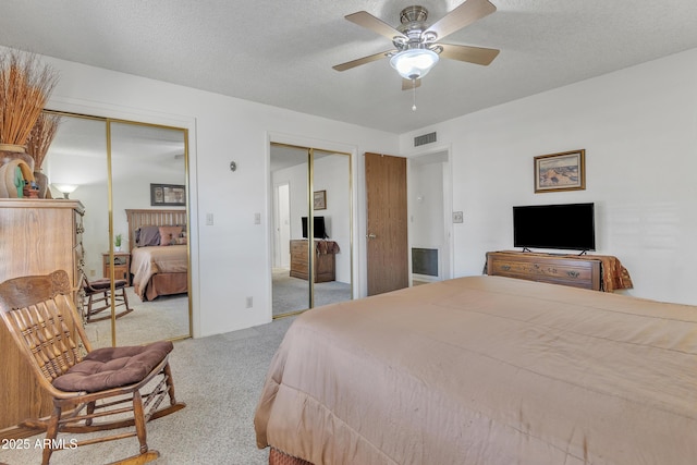 carpeted bedroom with ceiling fan, a textured ceiling, visible vents, and multiple closets