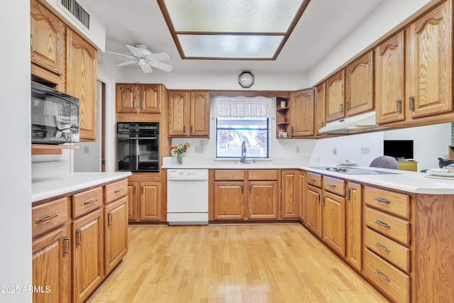 kitchen with visible vents, light wood-style floors, a sink, under cabinet range hood, and black appliances