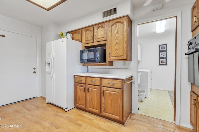 kitchen featuring light wood-style flooring, separate washer and dryer, visible vents, brown cabinets, and black appliances