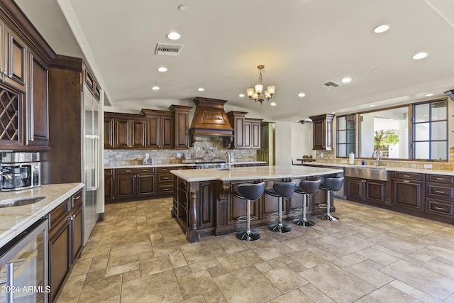 10125 E Cortez Dr, Scottsdale, AZ 85260 - kitchen featuring custom exhaust hood, wine cooler, backsplash, stone tile flooring, and a chandelier