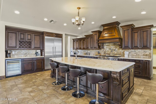 10125 E Cortez Dr, Scottsdale, AZ 85260 - kitchen with beverage cooler, appliances with stainless steel finishes, custom range hood, stone tile flooring, and decorative backsplash