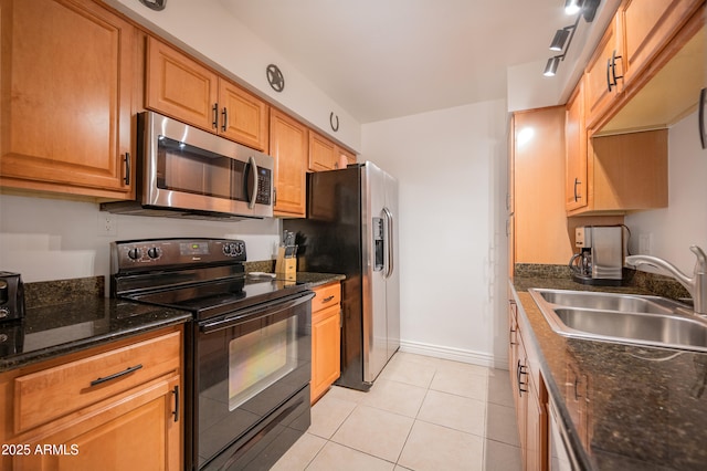 kitchen with dark stone counters, rail lighting, sink, light tile patterned floors, and stainless steel appliances