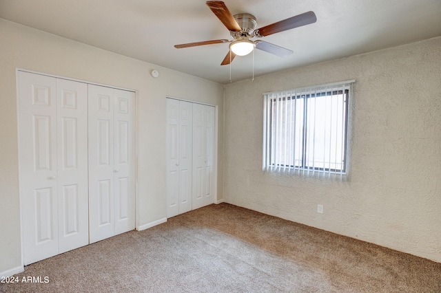 unfurnished bedroom with carpet flooring, ceiling fan, and multiple closets