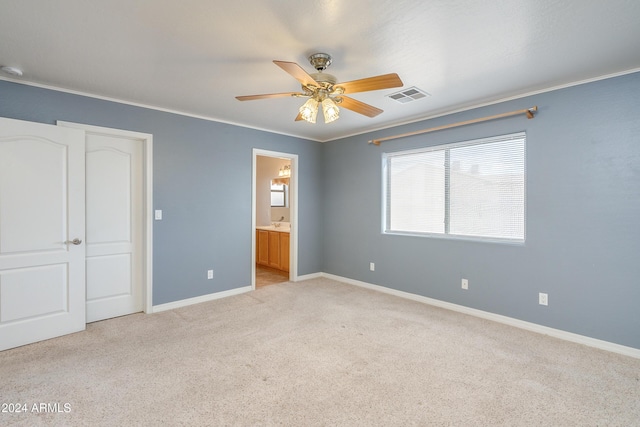 unfurnished bedroom featuring light colored carpet, ceiling fan, crown molding, ensuite bath, and a closet