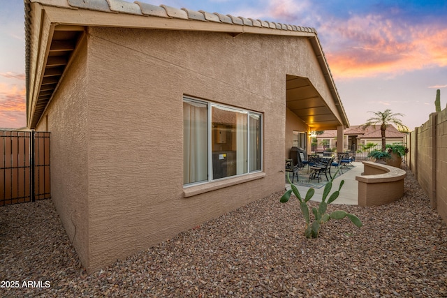 property exterior at dusk featuring a patio area, a fenced backyard, a tiled roof, and stucco siding