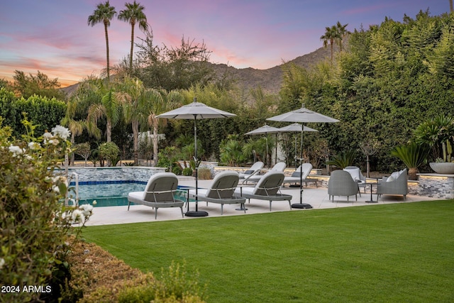 pool at dusk with a patio, a lawn, a fire pit, and a mountain view