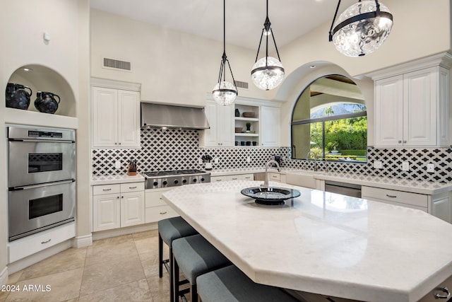 kitchen with sink, an island with sink, wall chimney range hood, white cabinetry, and appliances with stainless steel finishes