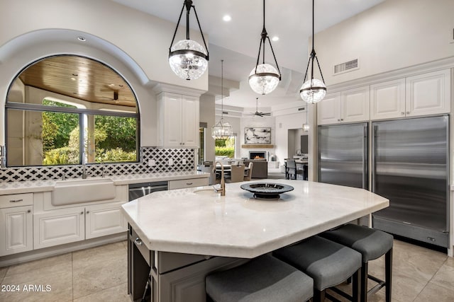 kitchen featuring hanging light fixtures, sink, white cabinets, stainless steel built in refrigerator, and a kitchen island with sink