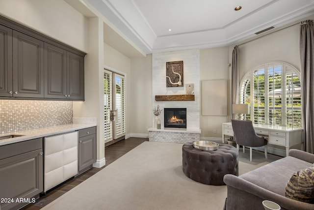 living room featuring dark hardwood / wood-style flooring, a raised ceiling, a healthy amount of sunlight, and a fireplace