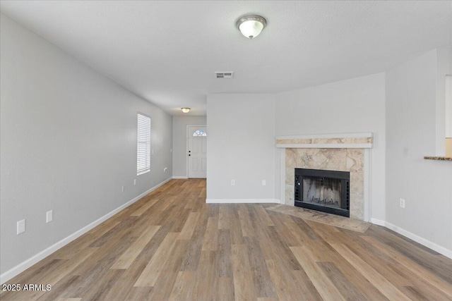 unfurnished living room featuring visible vents, baseboards, wood finished floors, and a tile fireplace