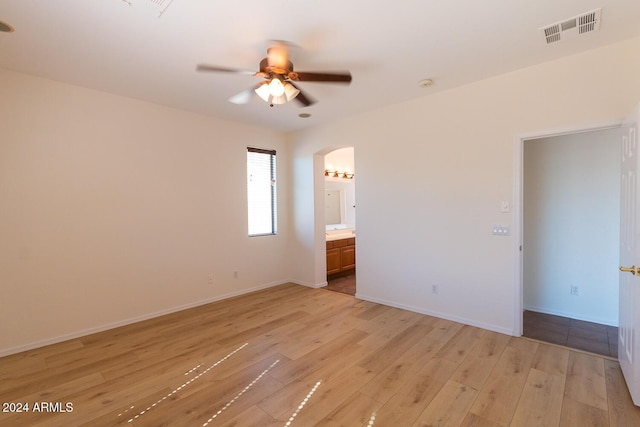 unfurnished bedroom with arched walkways, visible vents, light wood-style flooring, connected bathroom, and baseboards