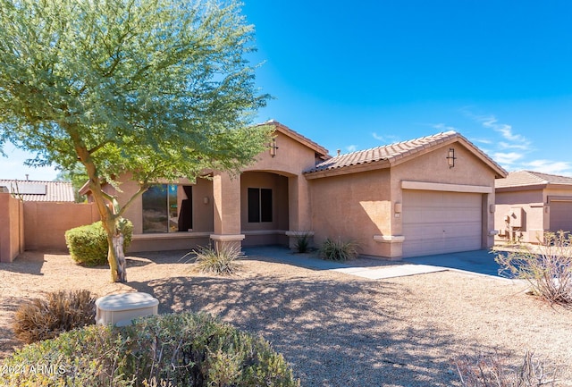 mediterranean / spanish-style house featuring a tile roof, stucco siding, an attached garage, fence, and driveway