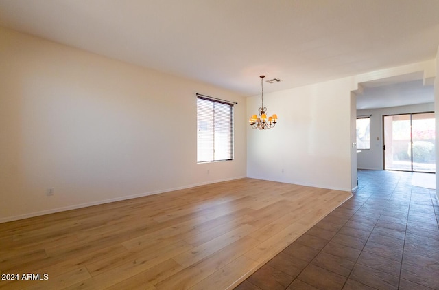 unfurnished room featuring baseboards, visible vents, a notable chandelier, and wood finished floors