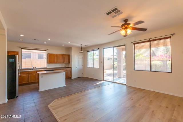 kitchen featuring visible vents, freestanding refrigerator, open floor plan, a kitchen island, and a sink