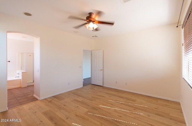 unfurnished bedroom featuring light wood finished floors, baseboards, arched walkways, and connected bathroom