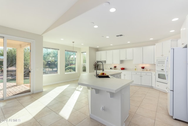 kitchen featuring light tile patterned flooring, decorative light fixtures, sink, a kitchen island with sink, and white appliances