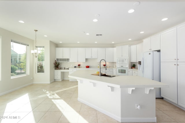 kitchen featuring a breakfast bar, sink, white cabinets, a large island with sink, and white appliances