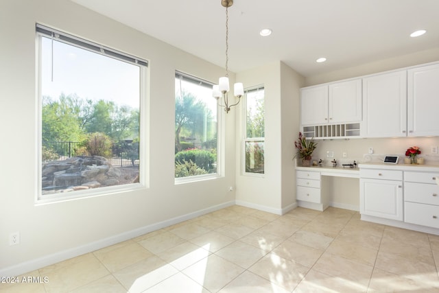 kitchen with hanging light fixtures, built in desk, light tile patterned floors, white cabinetry, and a chandelier