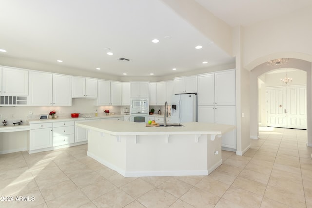 kitchen featuring white appliances, a spacious island, sink, white cabinetry, and a breakfast bar area