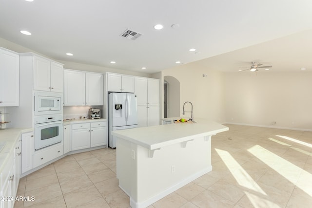 kitchen featuring ceiling fan, a kitchen breakfast bar, white appliances, a center island with sink, and white cabinets