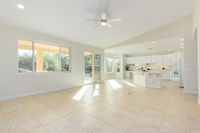 unfurnished living room featuring a healthy amount of sunlight, lofted ceiling, sink, and light tile patterned floors