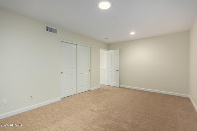 unfurnished bedroom with light colored carpet and a closet