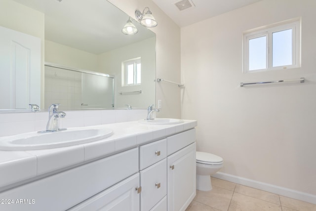 bathroom featuring tile patterned flooring, vanity, toilet, and a shower with shower door